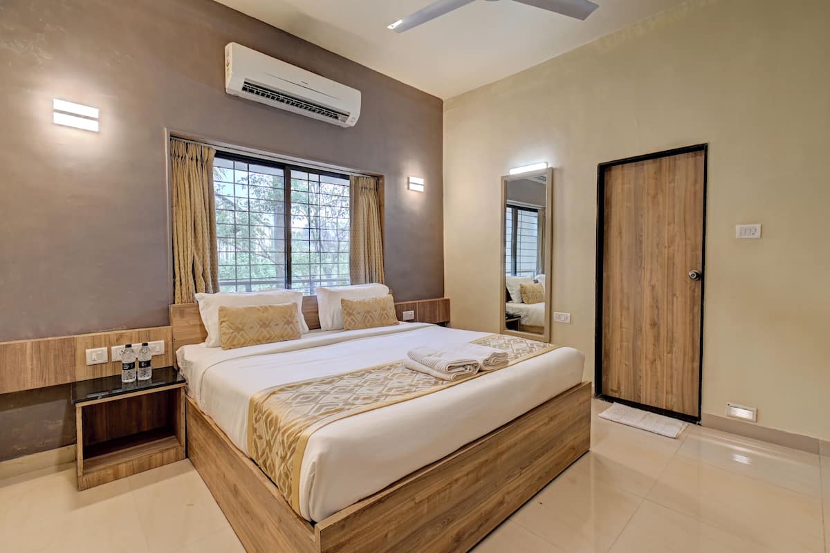 A modern bedroom with a large bed, wooden headboard, bedside tables with bottles, an air conditioner, and a mirror on the wall.