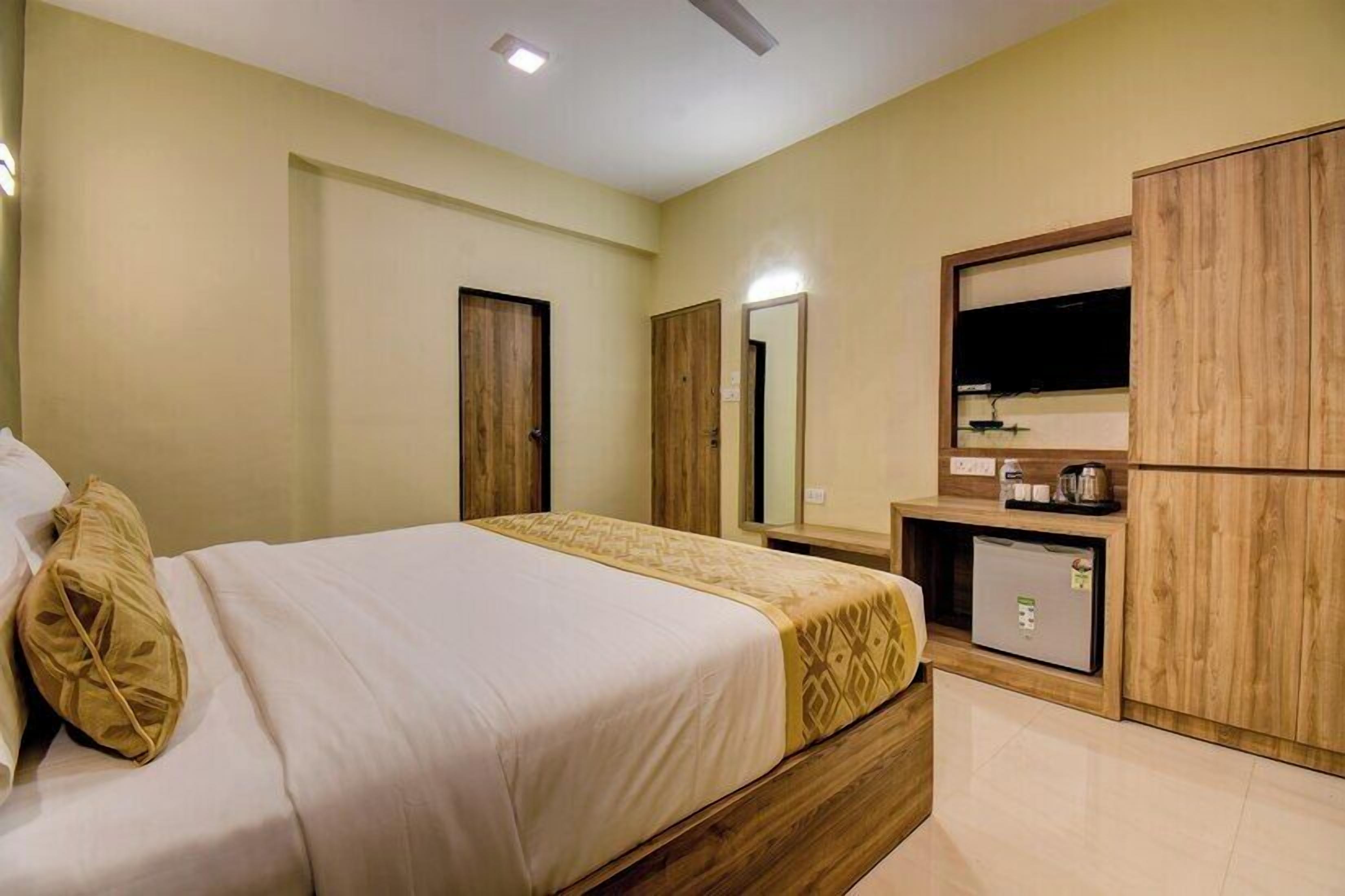 A hotel room with a bed, wooden wardrobe, a small kitchenette, and a mirror.