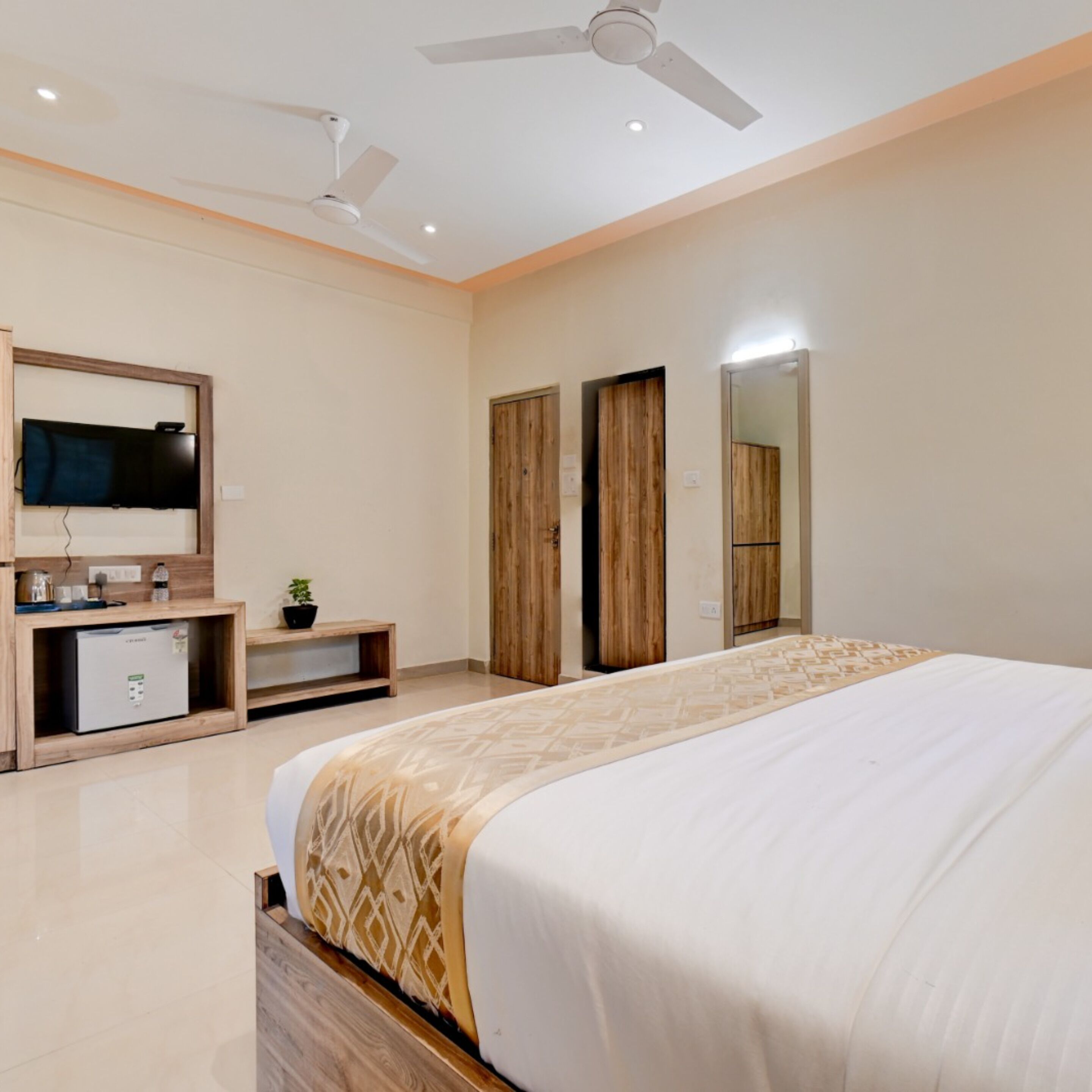 A modern bedroom with a large bed, a TV mounted on a wooden cabinet, and a ceiling fan.