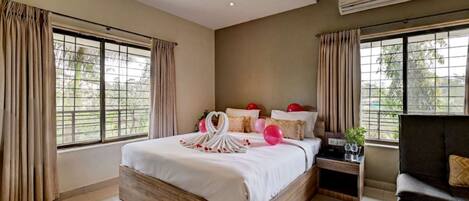 A hotel room with a large bed, a sofa, a nightstand, and a window with curtains.