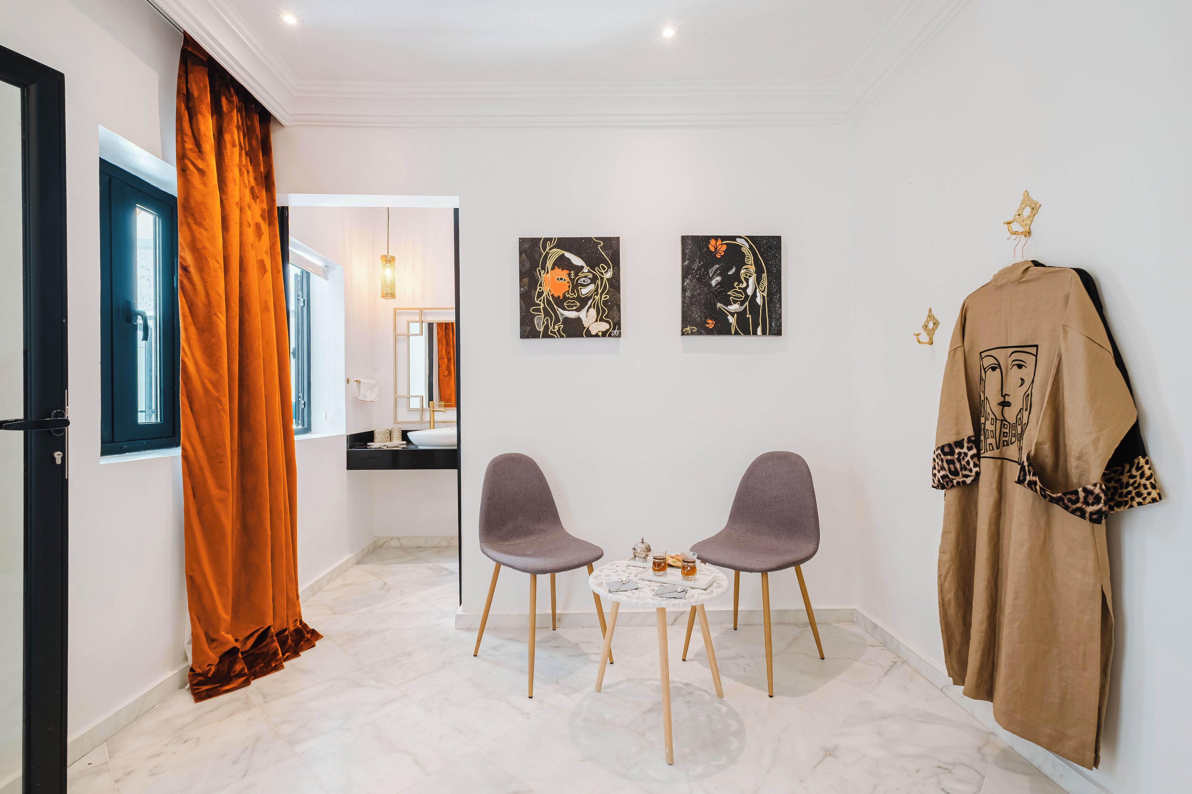 Een moderne kamer met twee grijze stoelen, een klein rond tafeltje en een kapstok met een bruin jas.