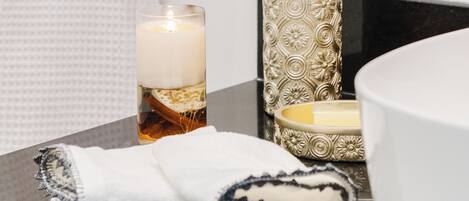 A bathroom with a black countertop, a white towel, a candle, and a soap dispenser.