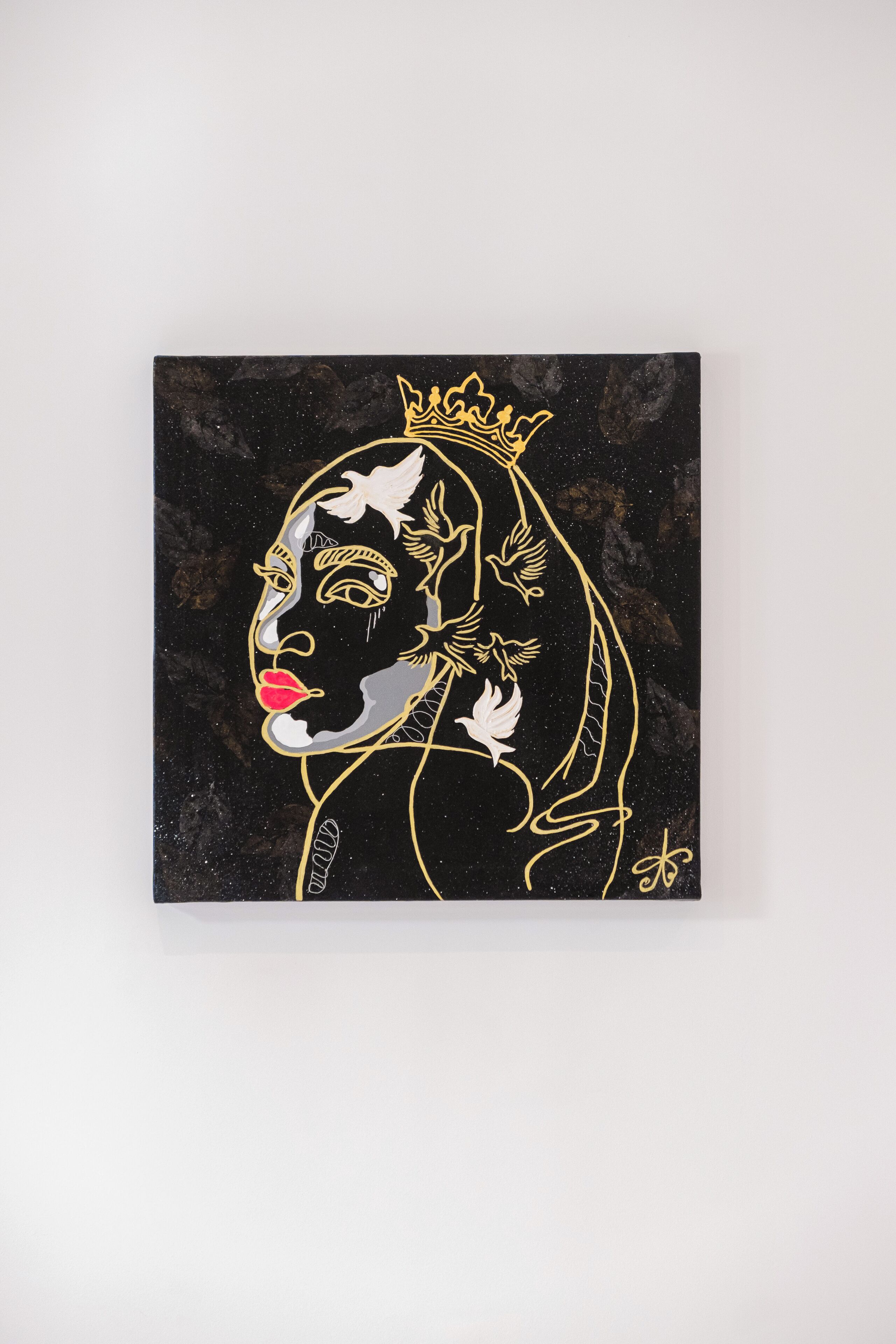 A framed artwork with a black background and gold outlines of a figure with a crown and birds.