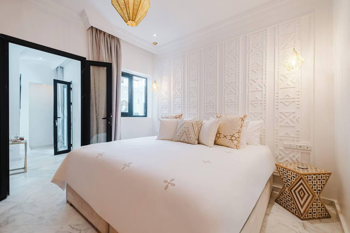 A spacious bedroom with a large bed, a glass door leading to a balcony, and a decorative wall panel.