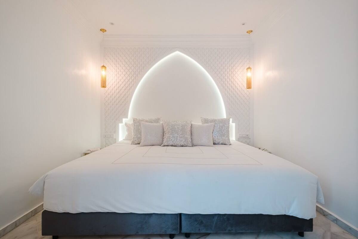 A modern bedroom with a large bed, a decorative ceiling light, and two wall-mounted lamps.