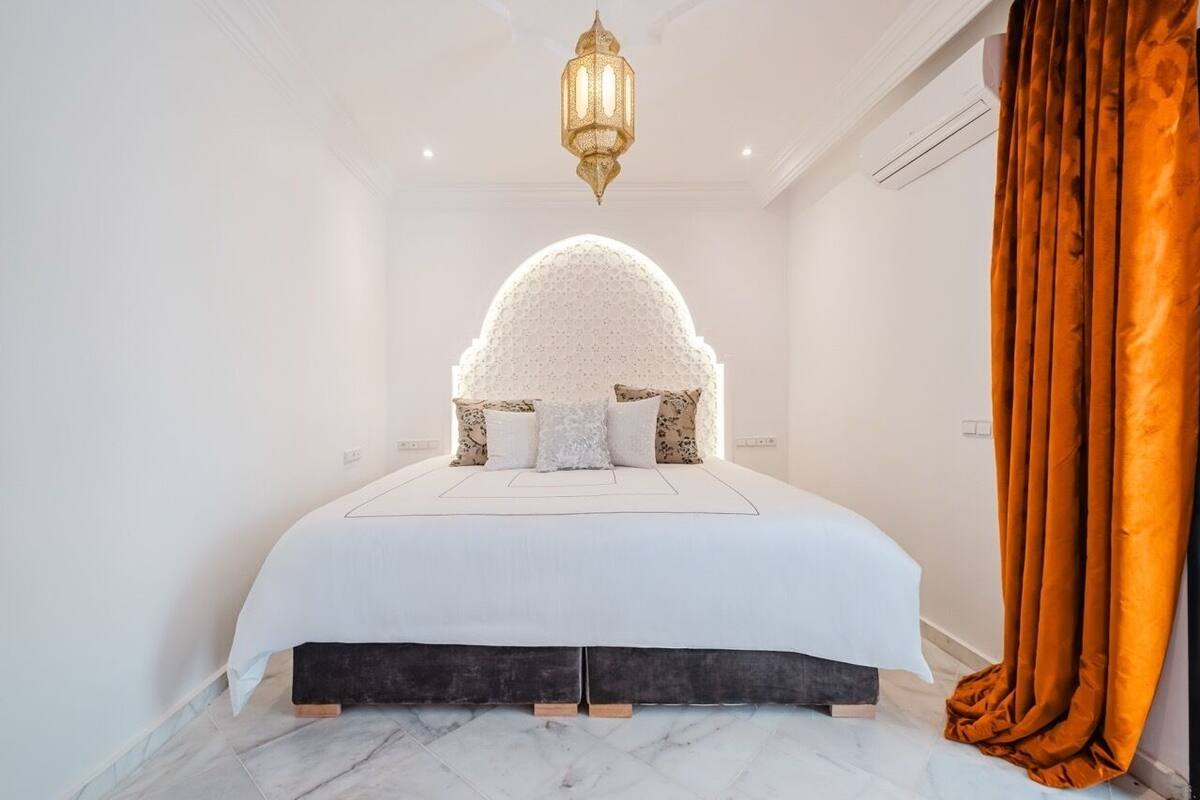 A bedroom with a large bed, a decorative arch, a hanging light fixture, and a curtain.
