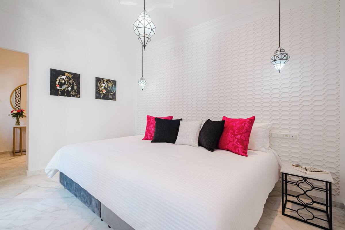 A modern bedroom with a large bed, white walls, and geometric patterned wallpaper.