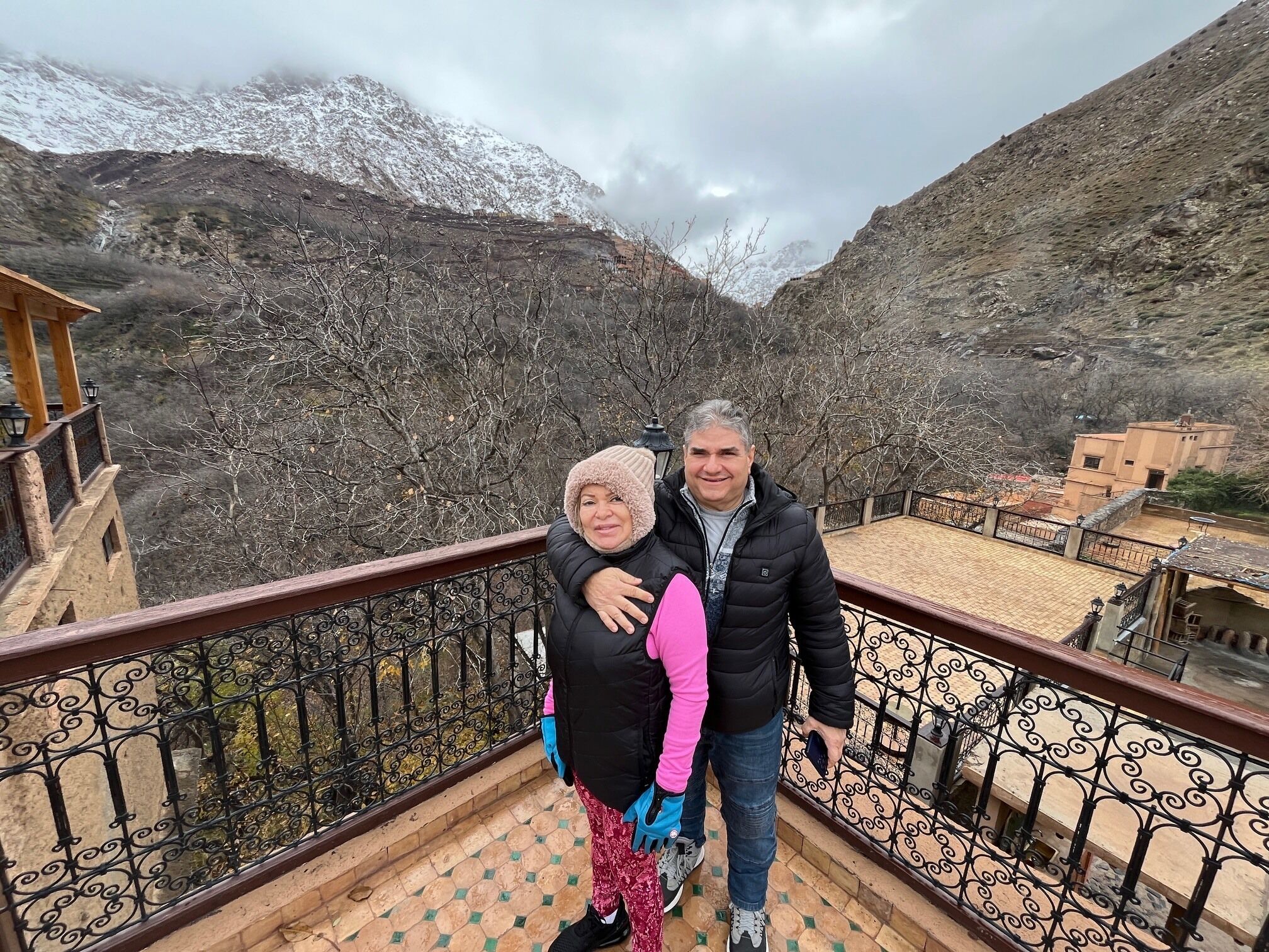 A couple standing on a balcony with a mountainous backdrop.