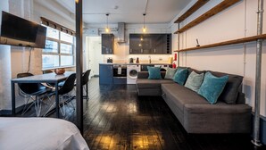 A modern kitchen with a built-in oven, microwave, and sink. There is a dining area with a table and chairs, and a sofa with cushions. - Stylish 1 Bedroom Flat - Sleeps 4 (London)