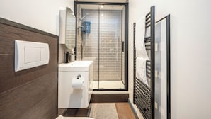 A modern bathroom with a glass shower enclosure, a white sink, and a towel rack. - Stylish 1 Bedroom Flat - Sleeps 4 (London)