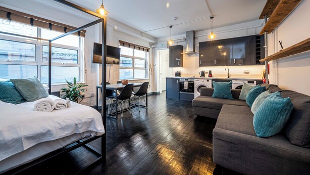 A modern, open-plan living space with a bed, sofa, dining area, and kitchen. - Stylish 1 Bedroom Flat - Sleeps 4 (London)