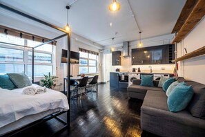 A modern, open-plan living space with a bed, sofa, dining area, and kitchen. - Stylish 1 Bedroom Flat - Sleeps 4 (London)