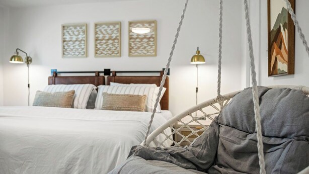 Une chambre à coucher avec un lit, un fauteuil suspendu et des œuvres d’art murales.