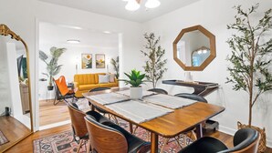 Un coin repas avec une table en bois, des chaises noires et un ventilateur de plafond. Un miroir est accroché au mur et une plante est posée sur la table.