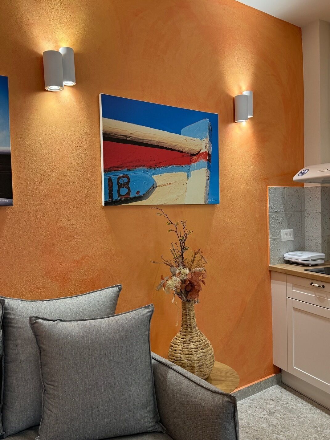 Una habitación con un sofá, un cuadro colgado en la pared, un jarrón con flores secas y una pequeña mesa.