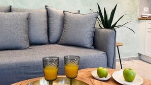 Un salon moderne avec un canapé gris, une œuvre d’art encadrée au-dessus, et un plateau contenant deux verres de jus d’orange sur une table en bois.
