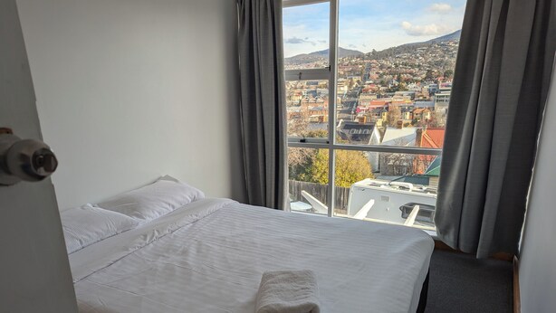 Habitación de hotel con una cama grande, ropa de cama blanca y vistas a un paisaje urbano a través de una ventana.