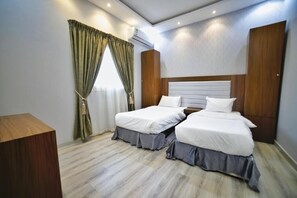 A hotel room with two beds, a wooden desk, and a window with curtains.