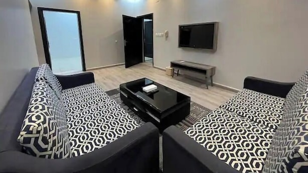 Una sala de estar moderna con un sofá, una mesa de centro, un televisor de pantalla plana y una puerta que da a otra habitación.