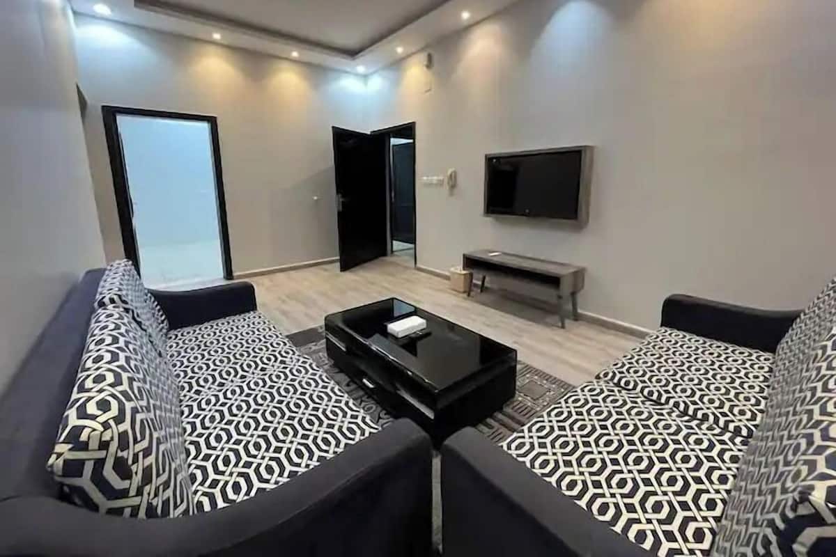 Un salon moderne comprenant un ensemble de canapés, une table basse, un téléviseur à écran plat et une porte donnant sur une autre pièce.