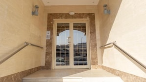 Entrada de hotel con pared de mármol, puerta de cristal con manija y barandillas metálicas a ambos lados.