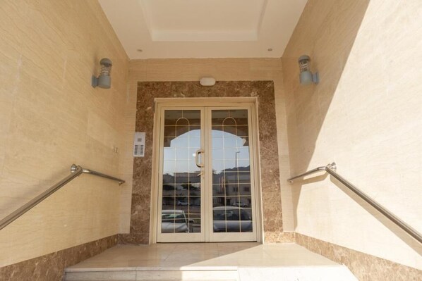 A hotel entrance with a marble wall, a glass door with a handle, and metal handrails on both sides.