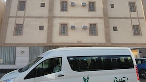 Una camioneta blanca estacionada frente a un edificio de varios pisos con fachada color crema y múltiples ventanas.