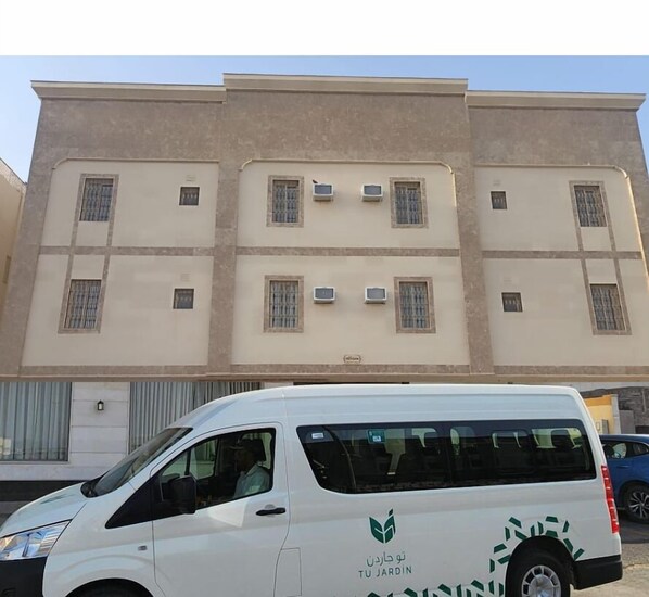 A white van parked in front of a multi-story building with a beige facade and multiple windows.
