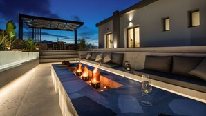 A modern outdoor seating area with a fire feature, a sofa, and a glass table. - Esotico Escape Villa (Kournas)