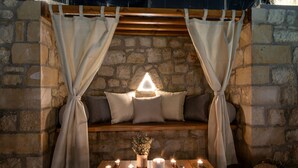 A cozy stone-walled seating area with a bench, cushions, and a table with candles. - Esotico Escape Villa (Kournas)