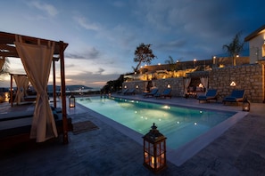 A swimming pool with lounge chairs and a pergola, surrounded by stone walls and a stone building. - Esotico Escape Villa (Kournas)