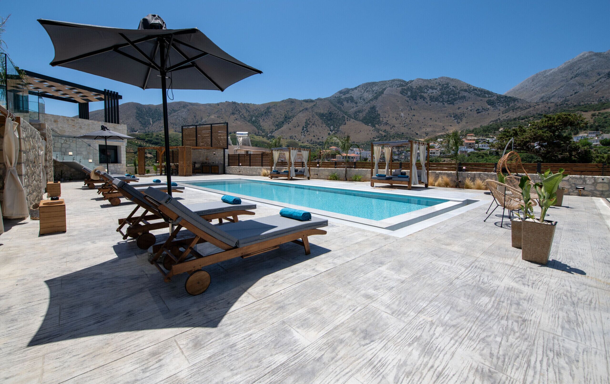 A pool area with lounge chairs, a pergola, and a view of mountains.
