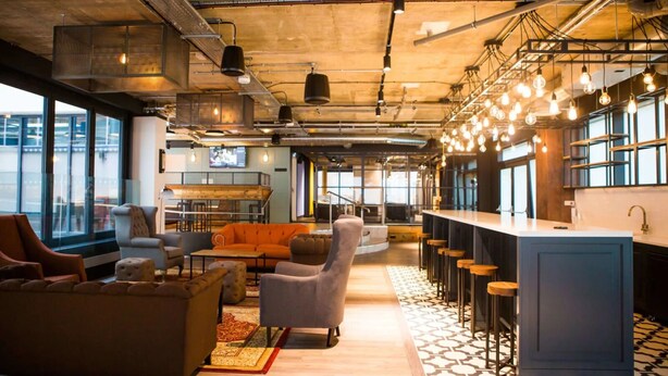 A modern lounge area with seating, a bar, and large windows. - Chapter Aldgate - Campus Accommodation (London)