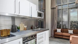A modern kitchen with stainless steel appliances, a built-in microwave, and a window with a city view. - Chapter Aldgate - Campus Accommodation (London)