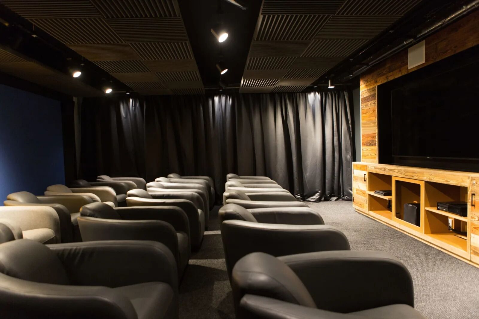 Un cine en casa con hileras de sillones reclinables, una pantalla grande y estanterías de madera.