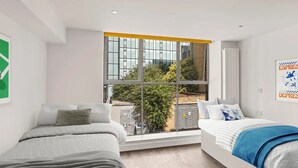 A modern hotel room with two beds, a large window with a view of the city, and a poster on the wall. - Chapter Aldgate - Campus Accommodation (London)