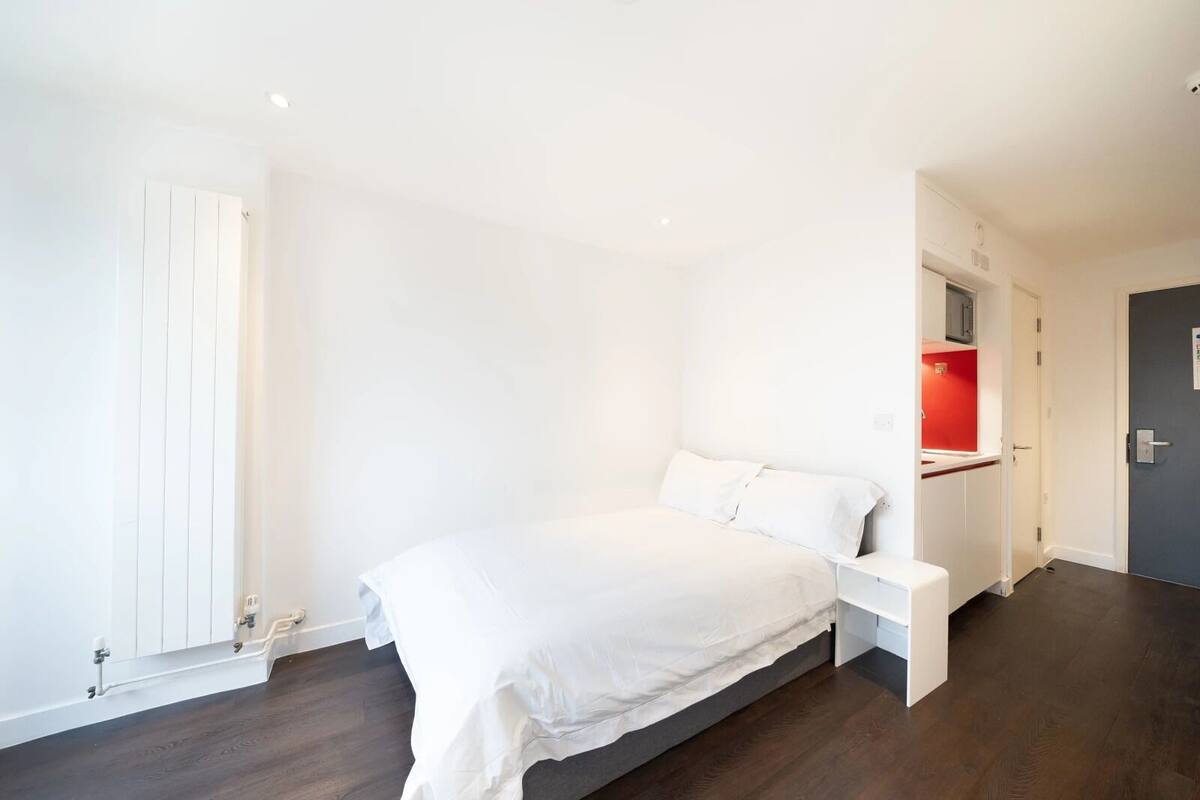 A bedroom with a bed, a white wardrobe, a red accent wall, and a door leading to a bathroom.