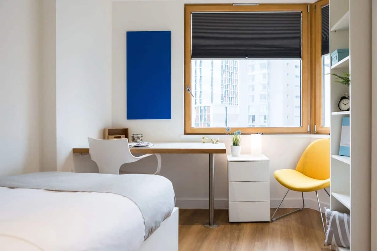 A modern bedroom with a bed, a desk, a chair, and a window with blinds.