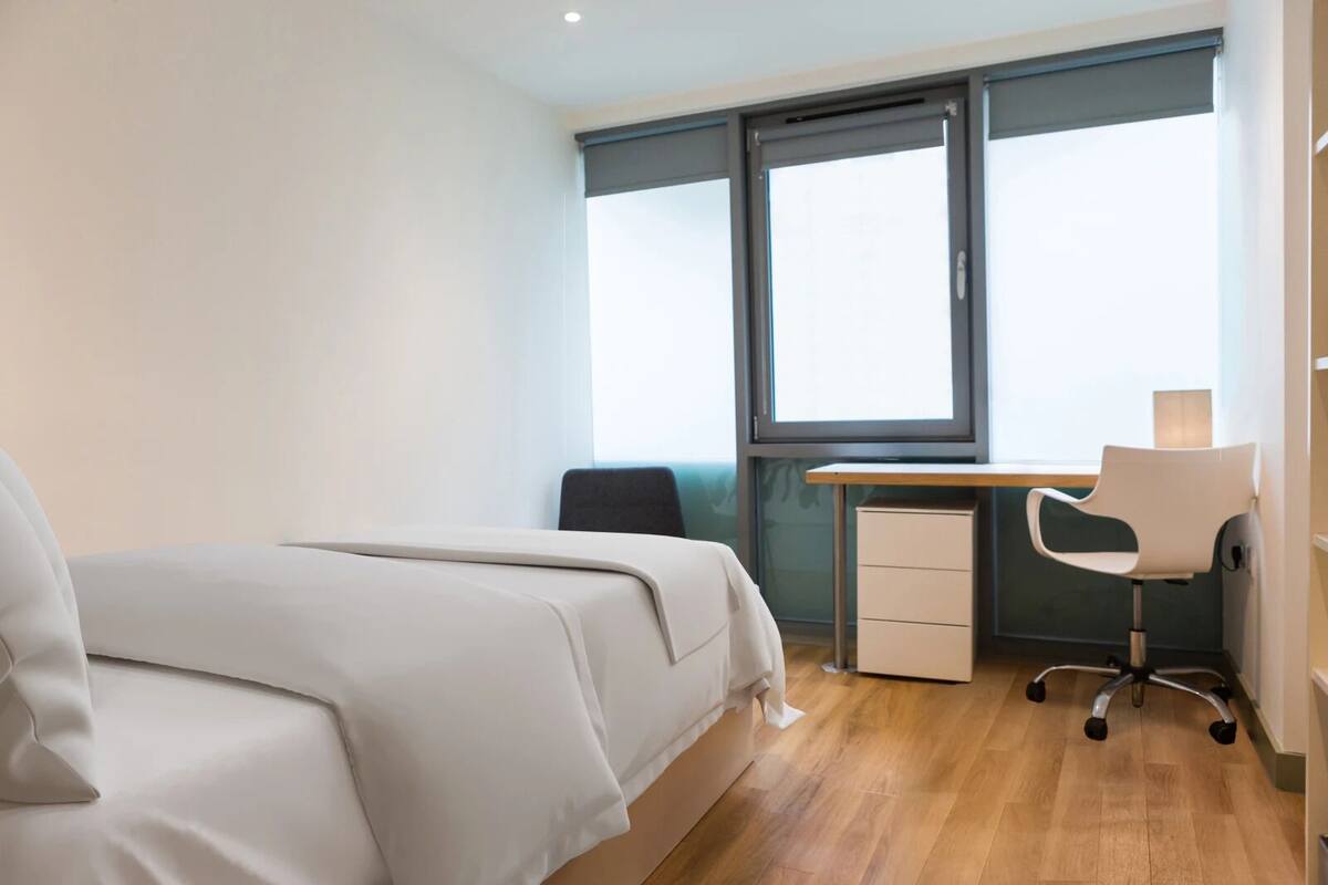 A bedroom with a bed, a desk, a chair, and a window.