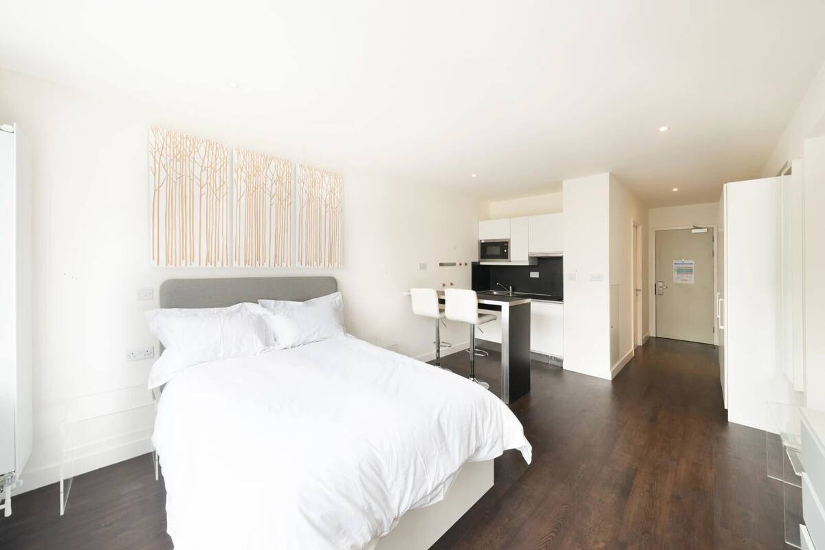 A modern hotel room with a large bed, a small kitchenette, and a separate bathroom.
