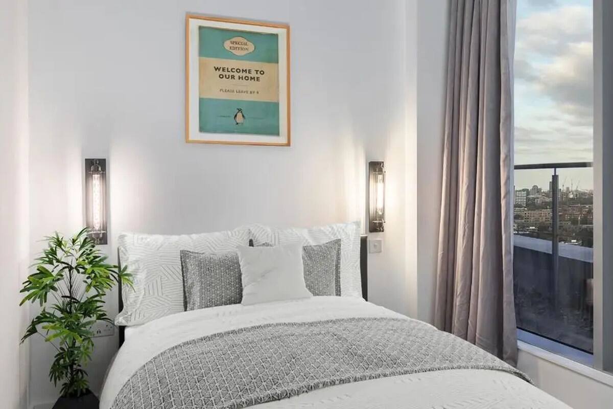 A modern bedroom with a city view, a framed welcome sign, and a large window with curtains.