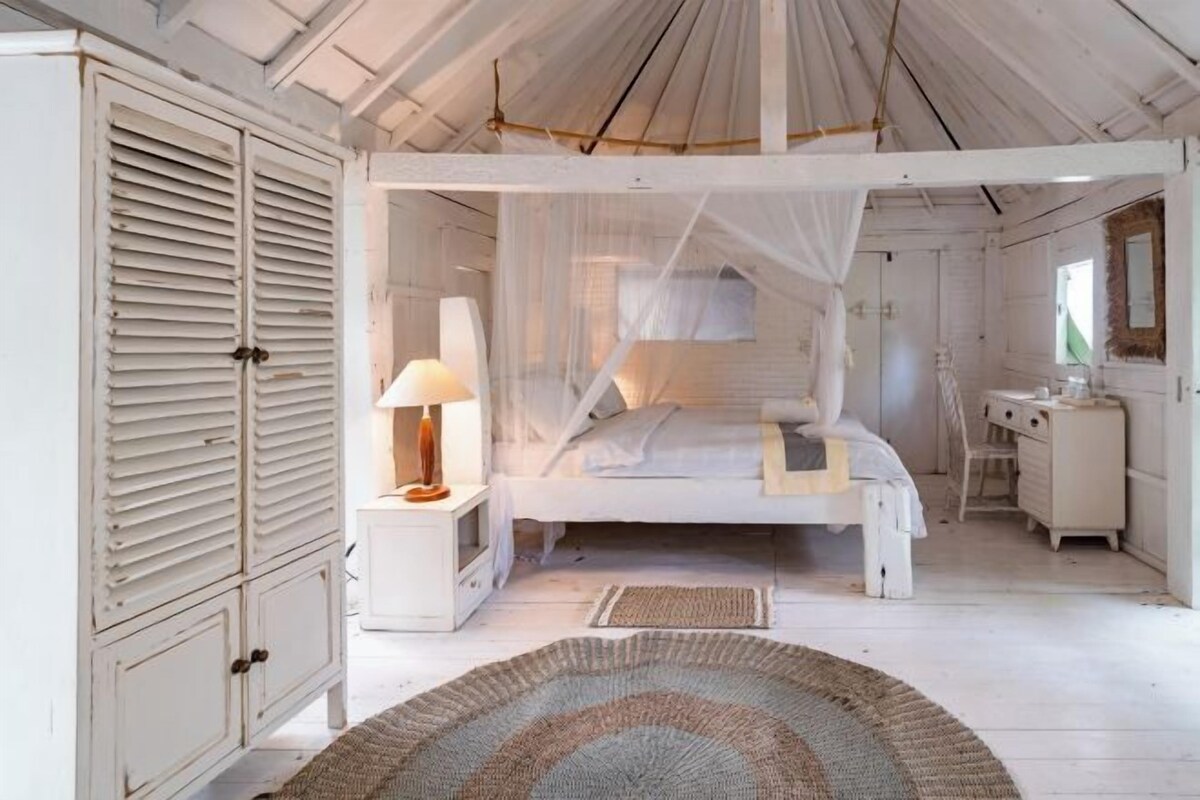 A white-themed bedroom with a canopy bed, bedside table, and a dresser.