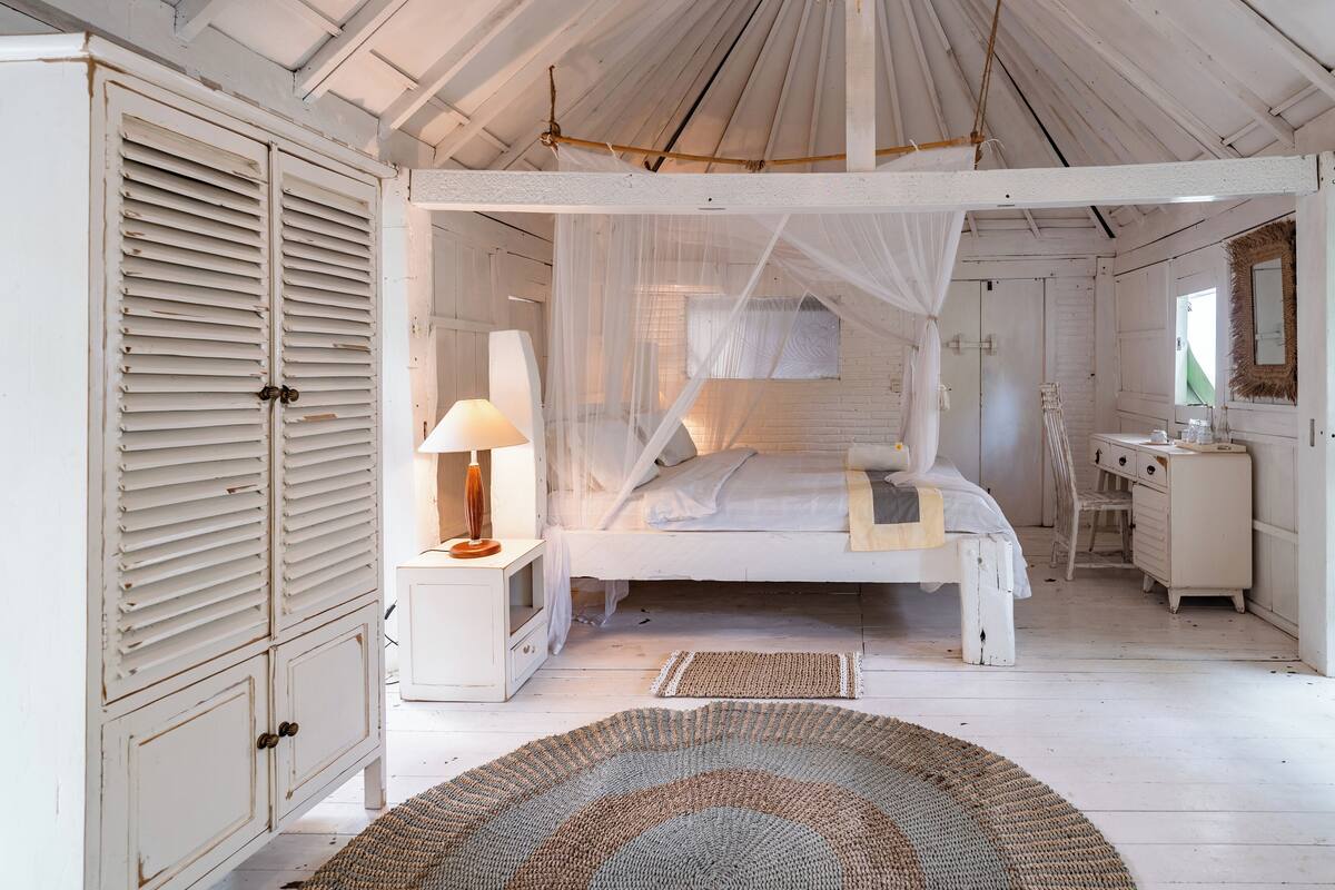 A bedroom with a canopy bed, a bedside table with a lamp, a dresser, and a mirror.