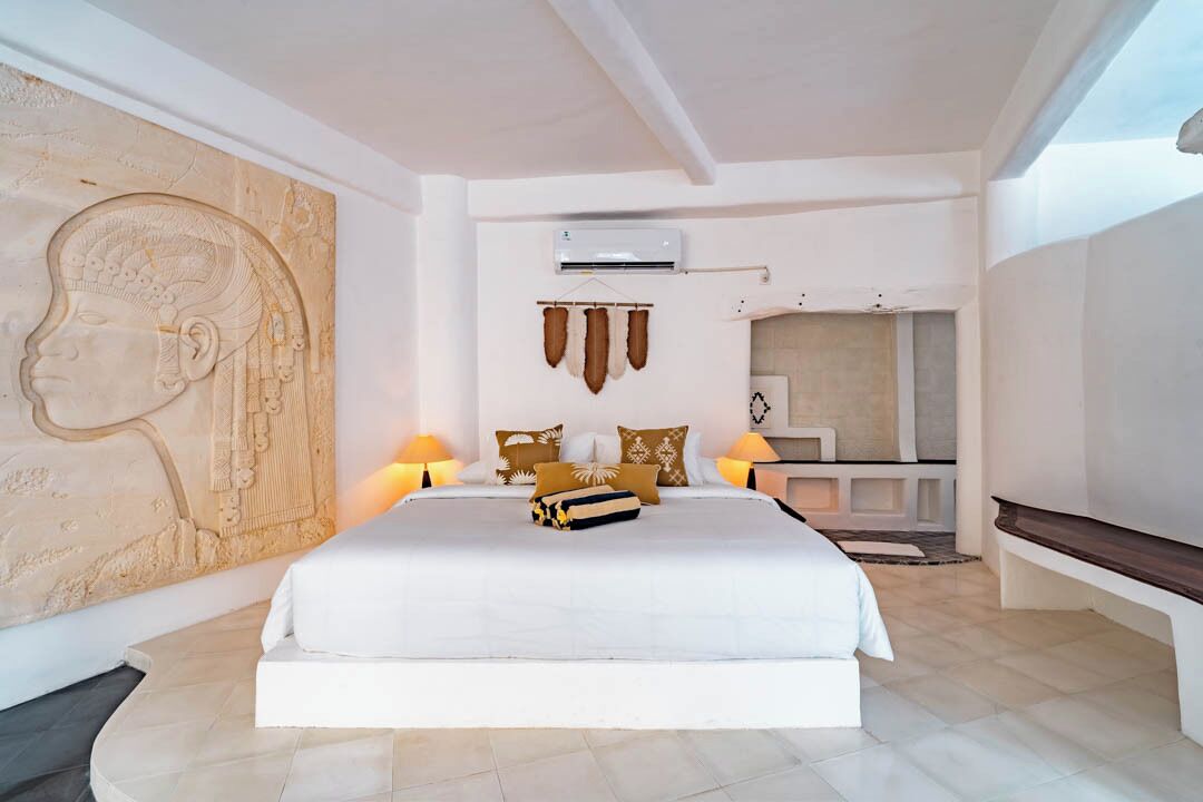 A modern bedroom with a large bed, a head sculpture on the wall, and a small TV on a stand.