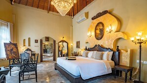 A bedroom with a large bed, a chandelier, a mirror, and a stone floor. - La Santa Rosa (Jimbaran)