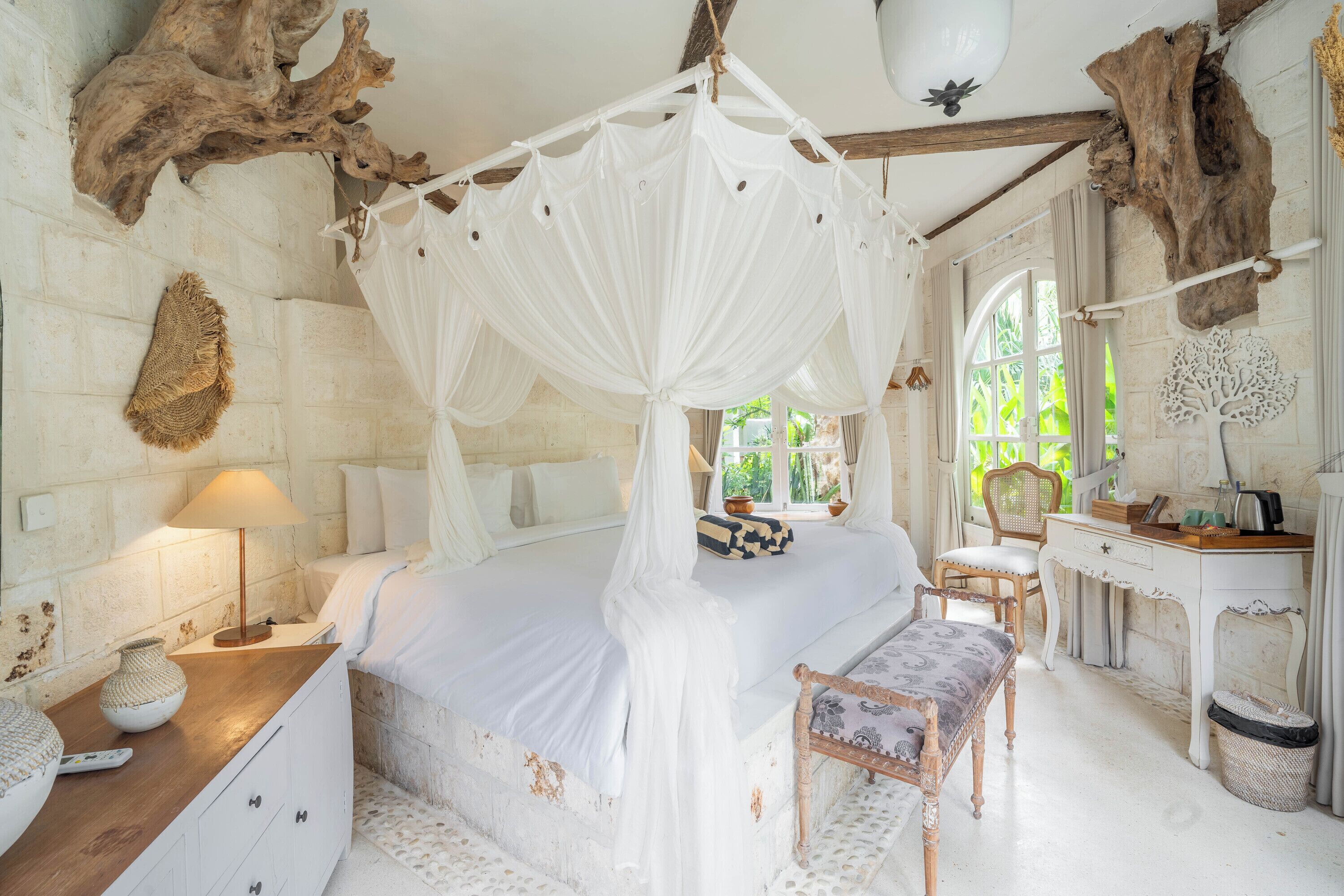 A bedroom with a canopy bed, a wooden desk, a chair, and a small table with a lamp.