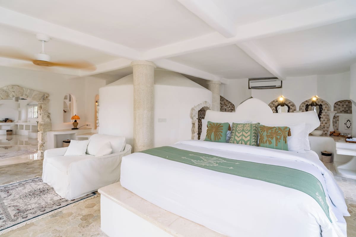 A spacious bedroom with a large bed, a sitting area with a white sofa, and a stone archway.