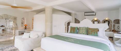 Un dormitorio amplio con una cama grande, una zona de estar con un sofá blanco y un arco de piedra.