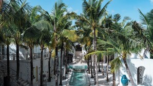 A pool area with palm trees, a blue vase, and a staircase leading to a building. - La Santa Rosa (Jimbaran)