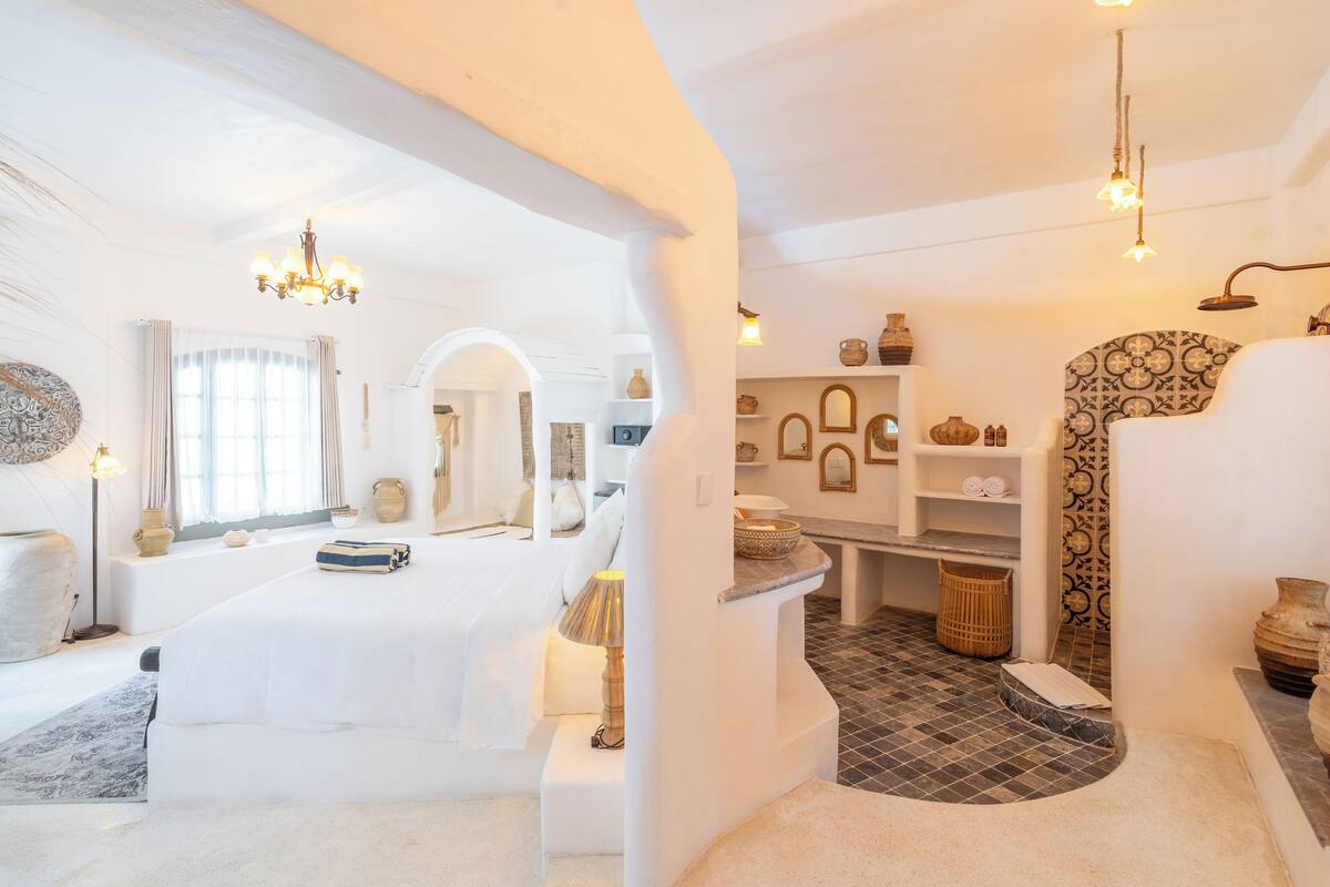 A spacious room with a large bed, a sitting area, and a bathroom with a shower and tiled floor.